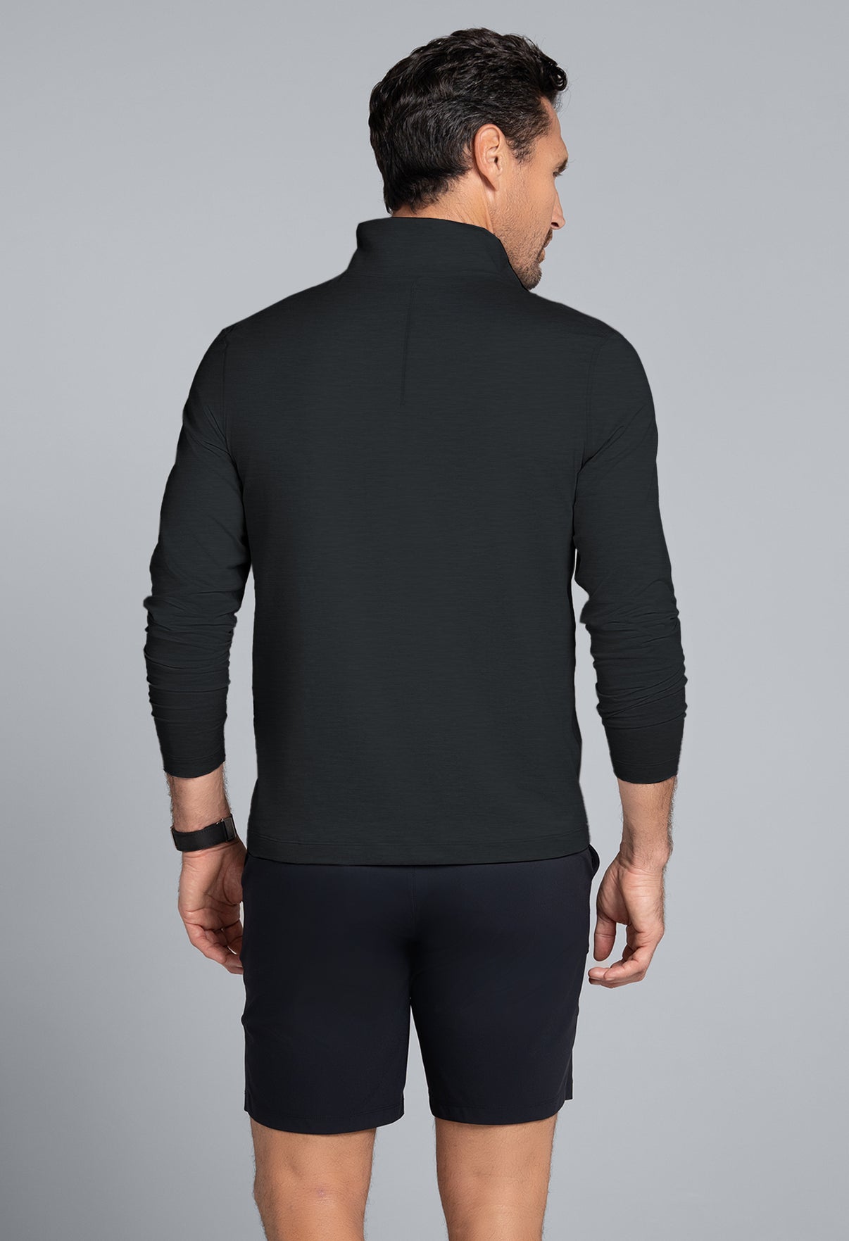 Man wearing a black long-sleeve shirt and black shorts on a gray background