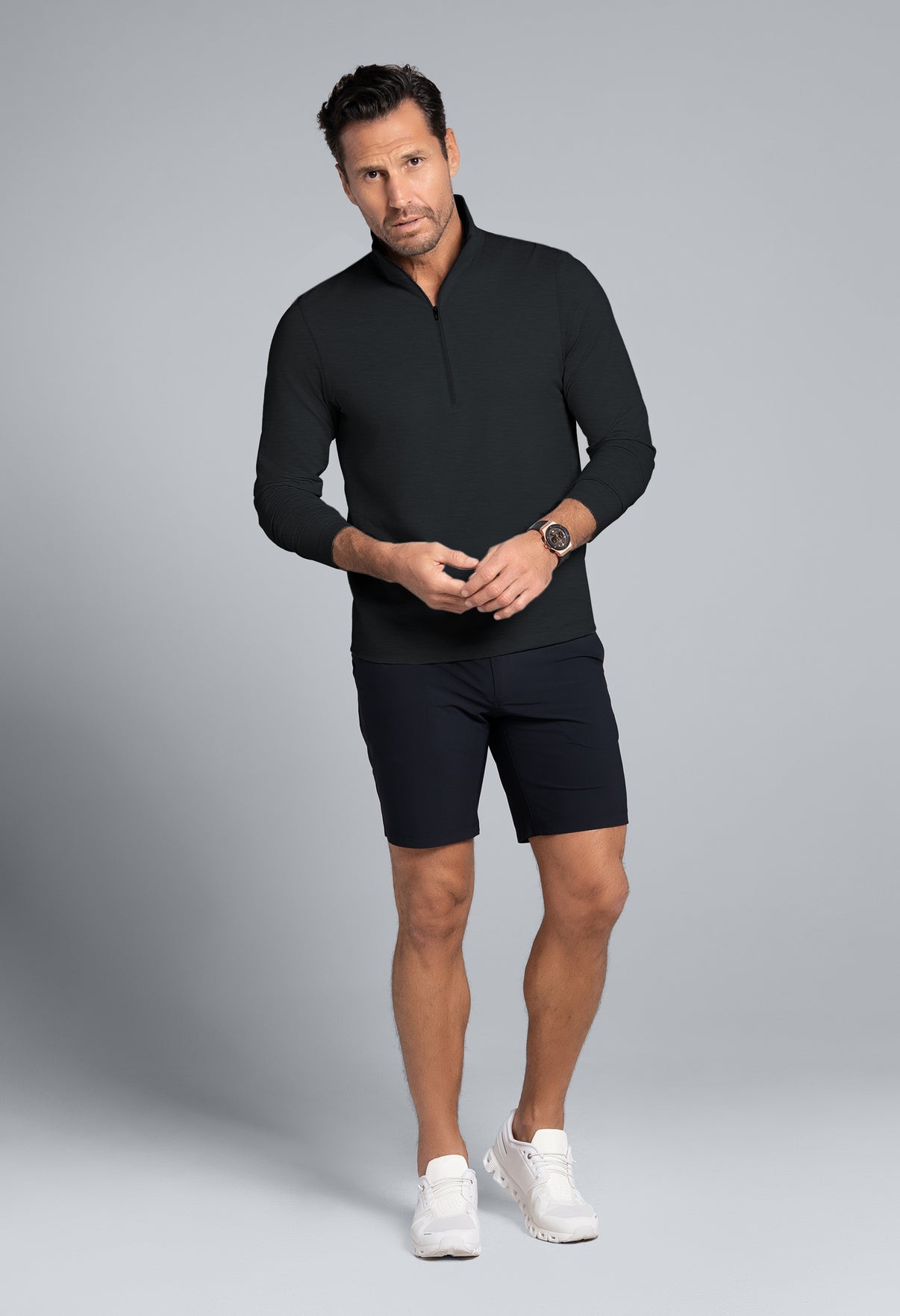 Man wearing a black long-sleeve shirt and black shorts on a gray background