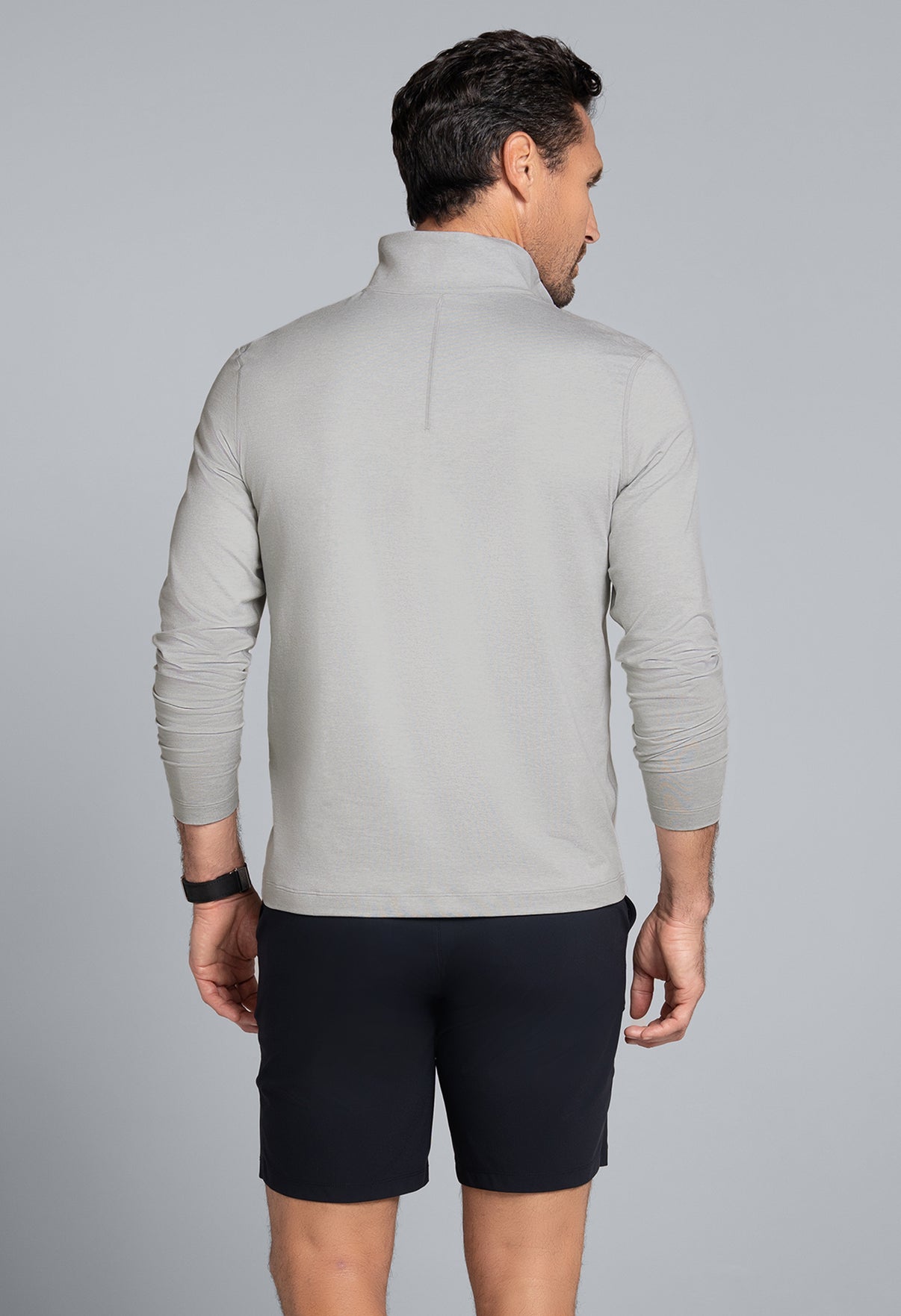 Man wearing a gray long-sleeve shirt and black shorts on a gray background