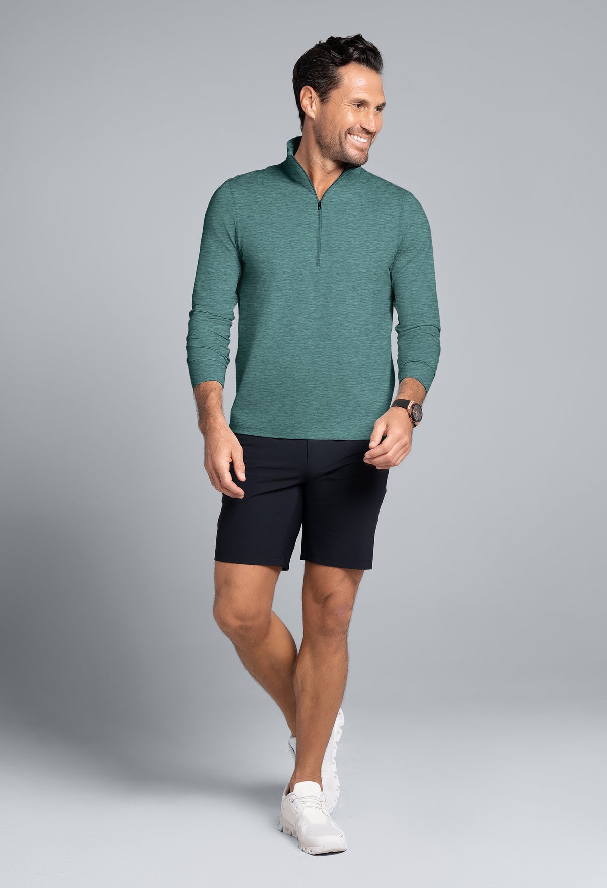 Man wearing a green long-sleeve shirt and black shorts on a gray background