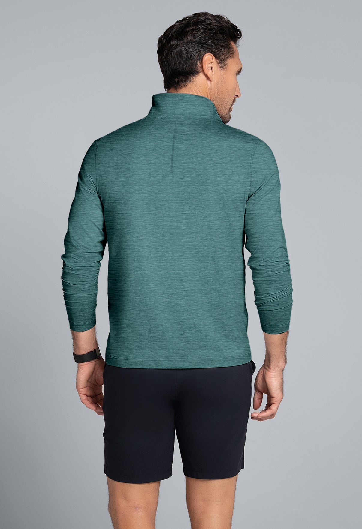 Man wearing a green long-sleeve shirt and black shorts on a gray background