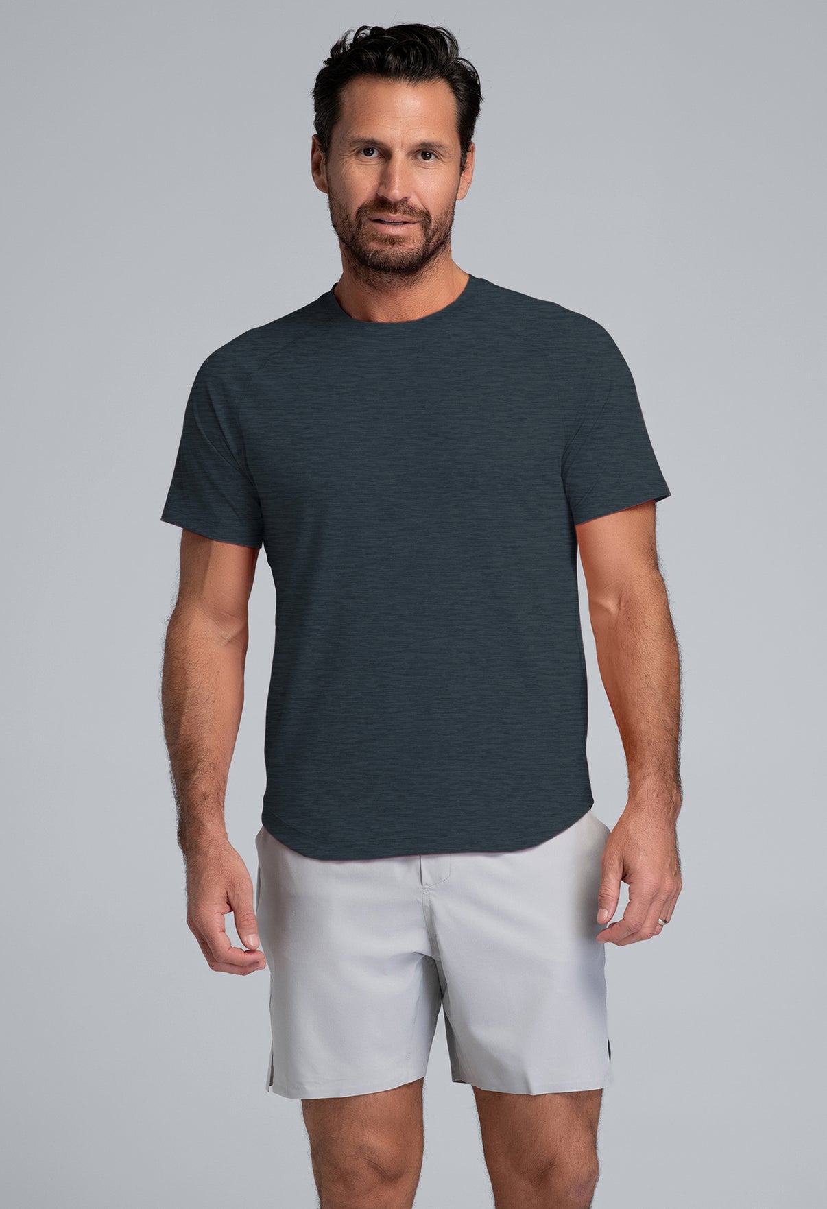 Man wearing a dark gray t-shirt and light gray shorts on a gray background