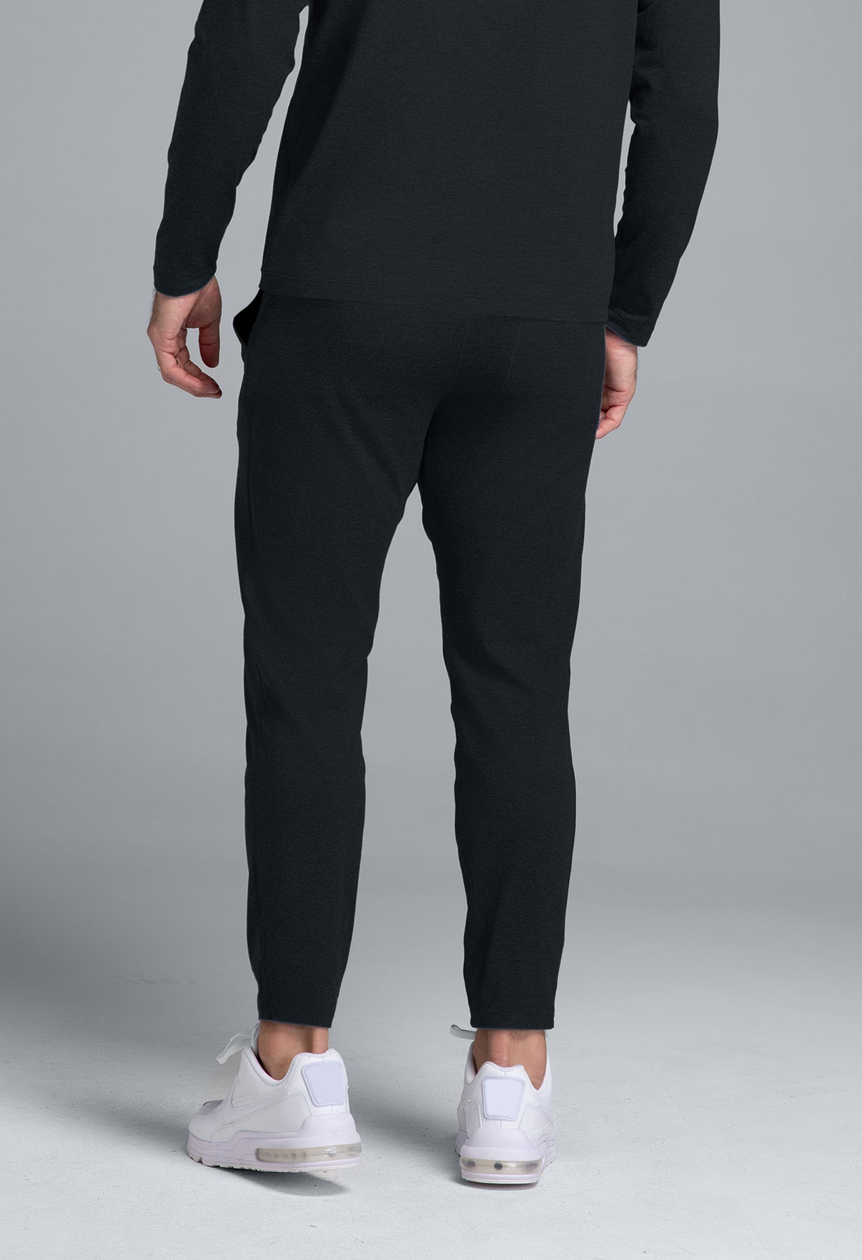 Person wearing black jogger pants and white sneakers on a gray background