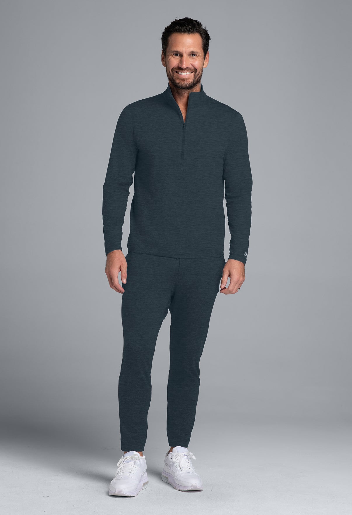 Man wearing a dark gray outfit with white sneakers on a gray background