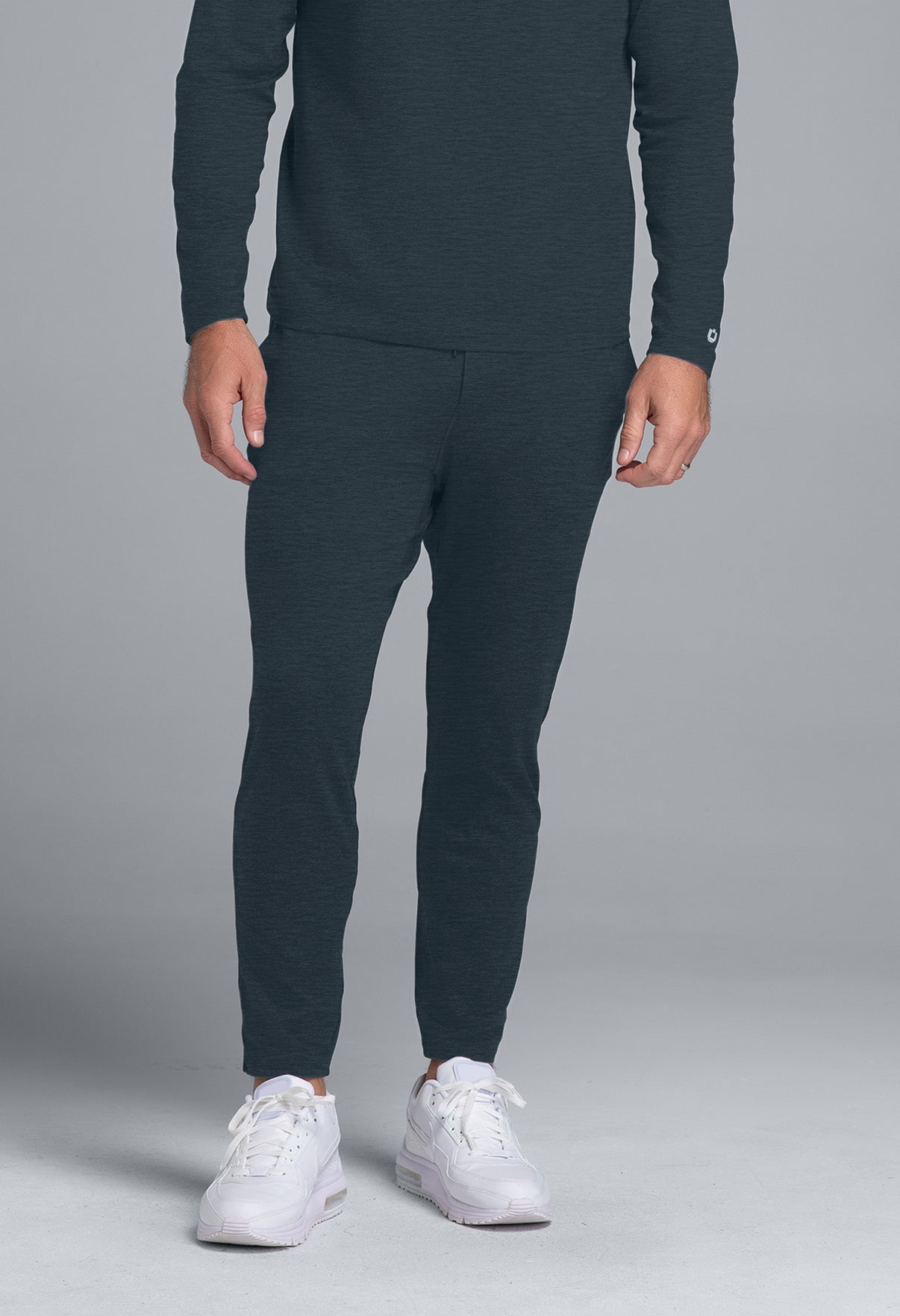 Person wearing dark gray jogger pants and white sneakers on a gray background