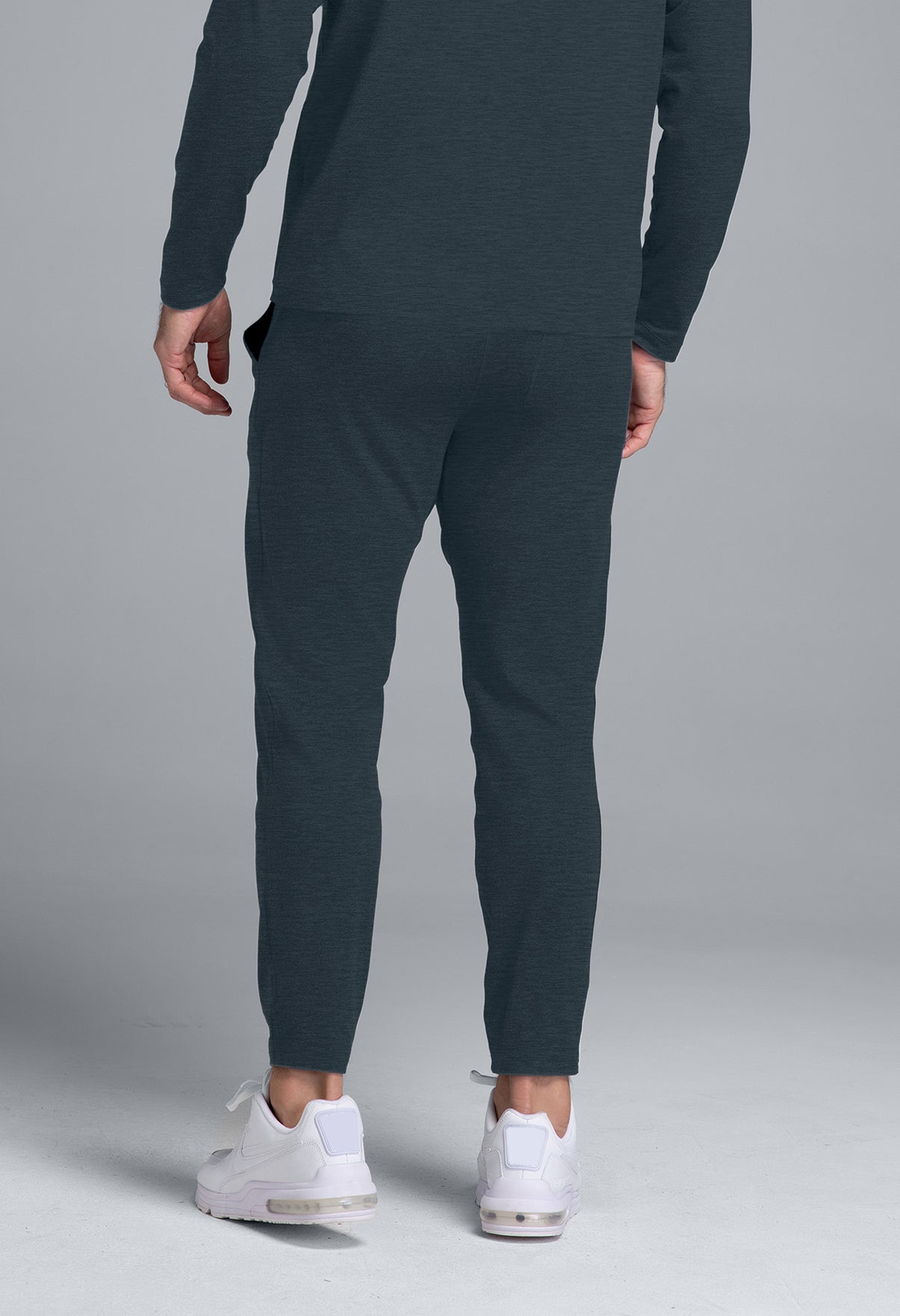 Person wearing dark gray jogger pants and white sneakers on a gray background