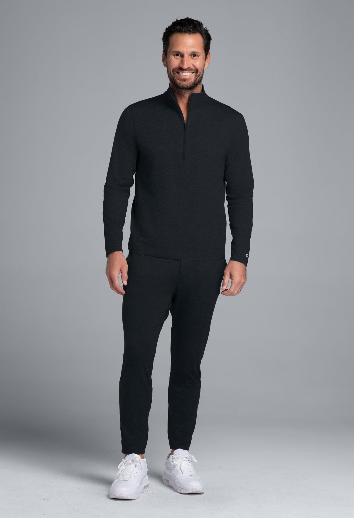 Man wearing a black outfit with white sneakers on a gray background