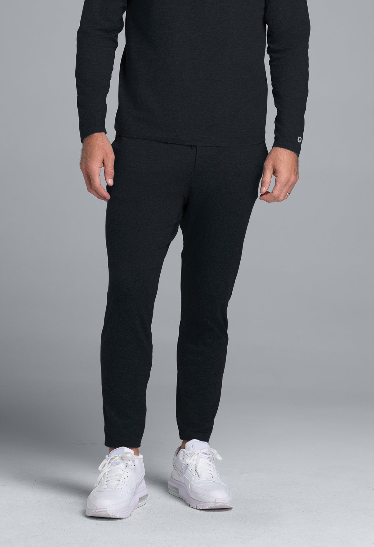 Person wearing a black outfit with white sneakers on a gray background